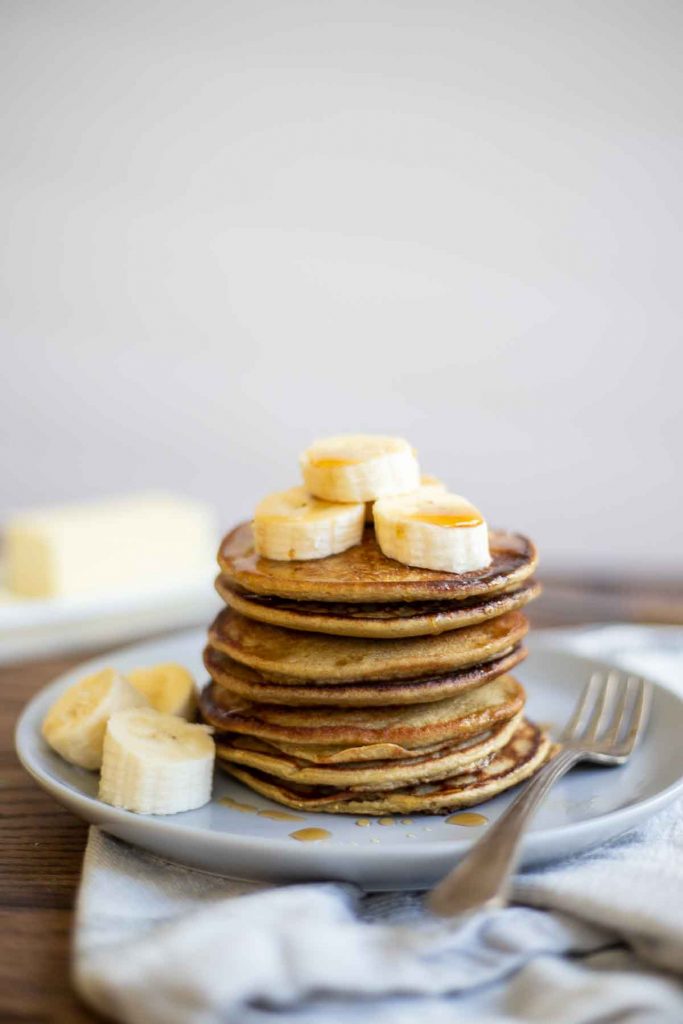 stack of banana protein pancakes on a gray plate and topped with sliced bananas