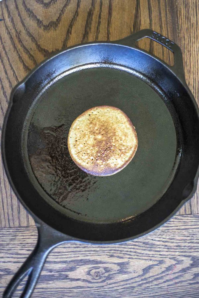 one banana protein pancake in the middle of a large cast iron pan on a wood cutting board