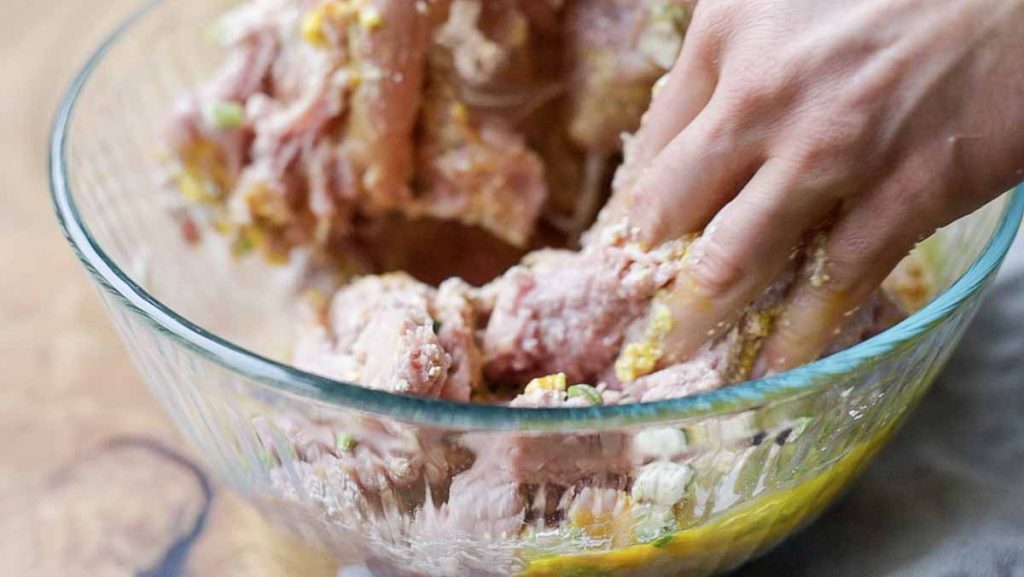 hands mixing ground turkey and other ingredients together in a glass bowl