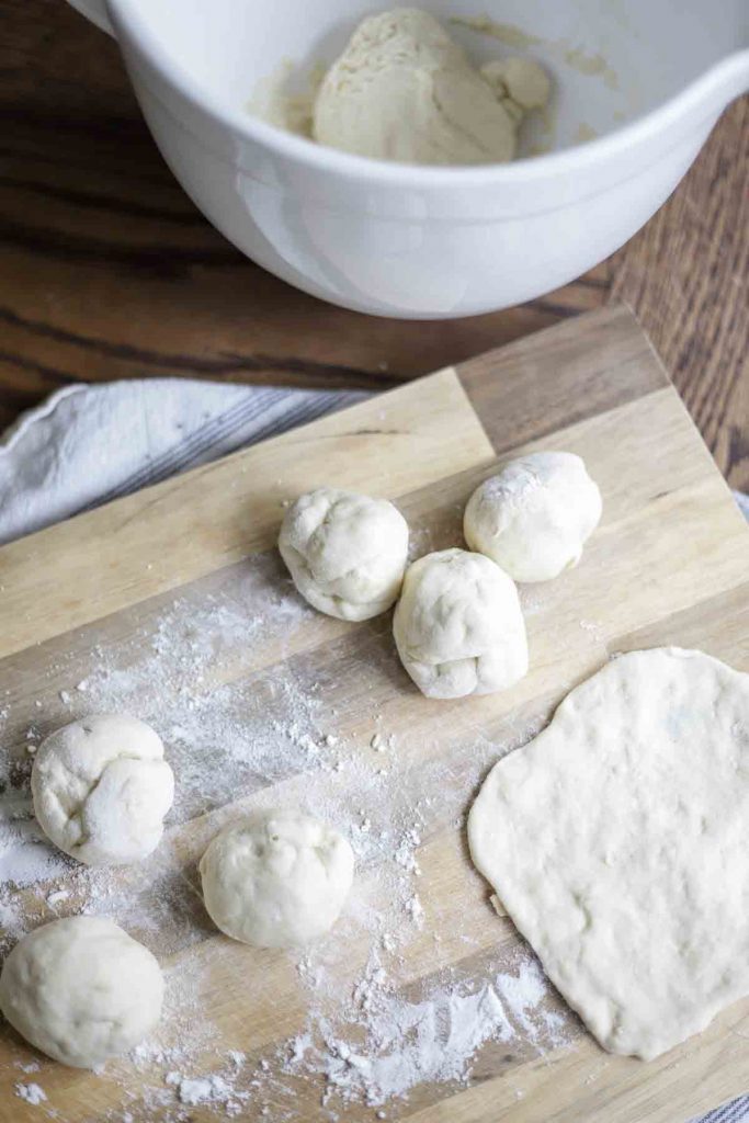 six balls of dough on a lightly floured cutting board with a white bowl in the background