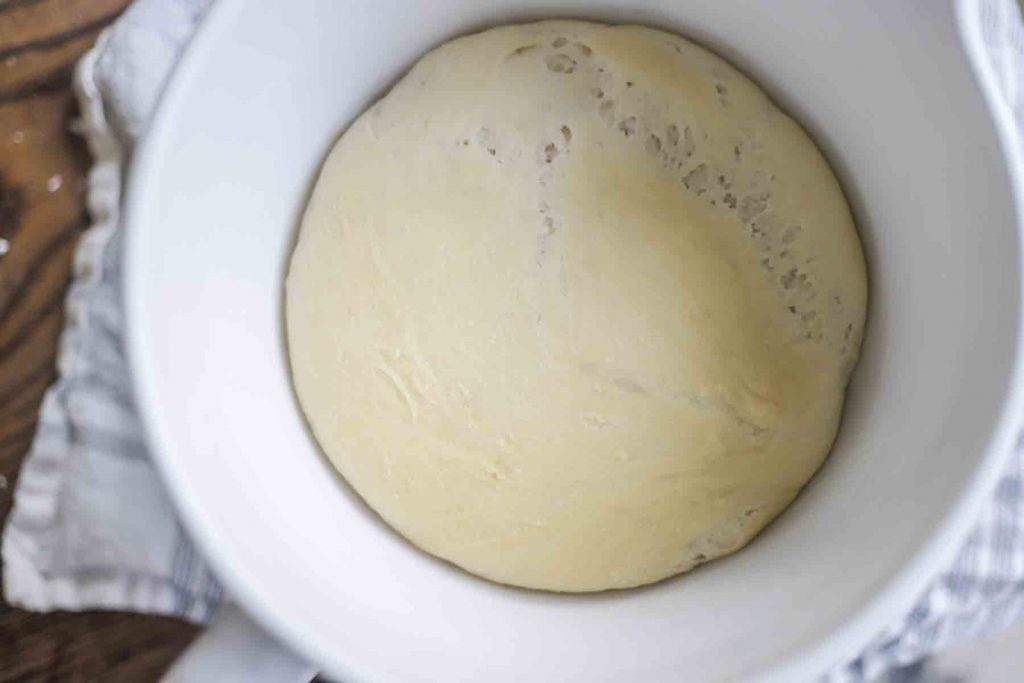 sourdough flatbread dough that has fermented overnight in a white ceramic stand mixer bowl on a white and blue stripped towel