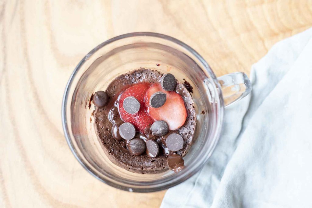 view from above of mug cake in clear mug with chocolate chips on top and strawberries
