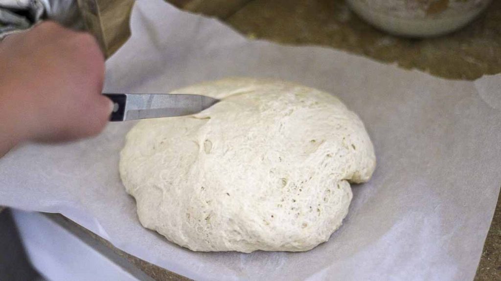 slicing sourdough discard bread dough with a knife on parchment paper