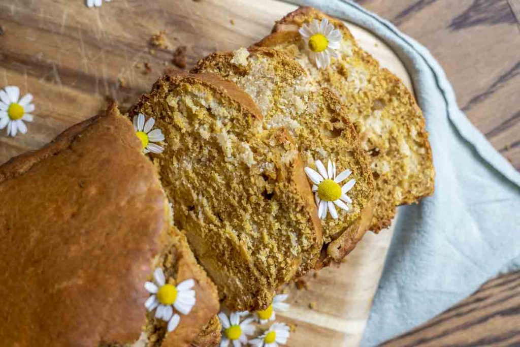 overhead photo of a sliced loaf of sourdough pumpkin bread topped with chamomile flowers