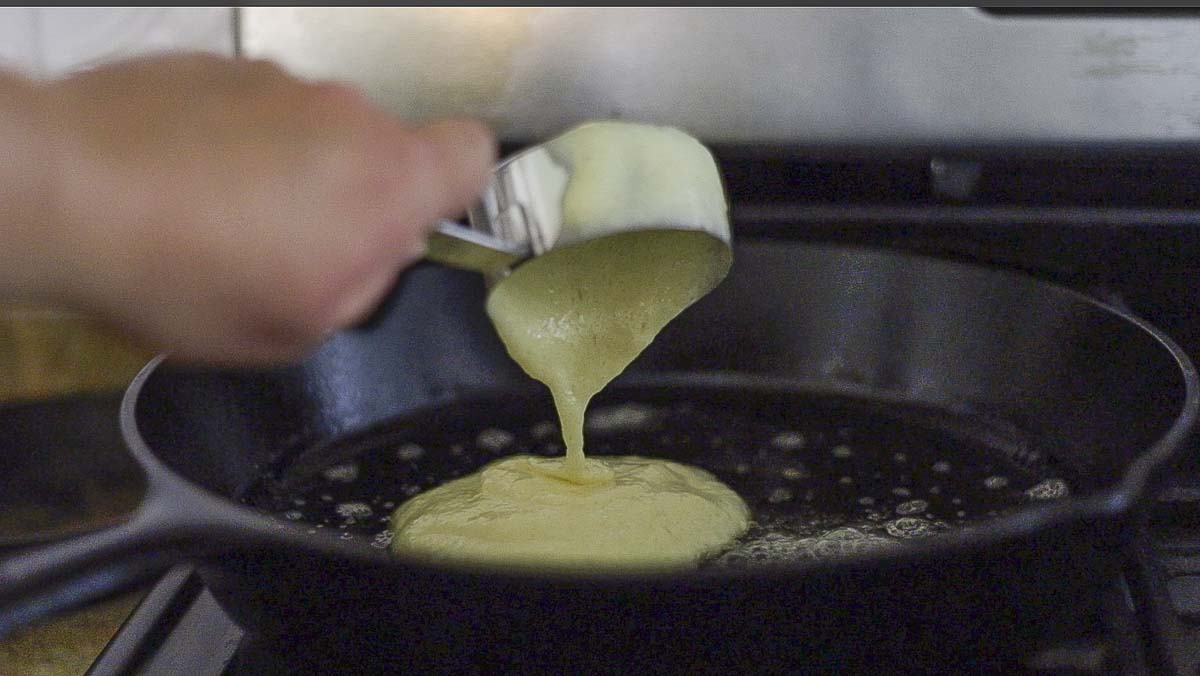 hand pouring pancake batter into a cast iron skillet