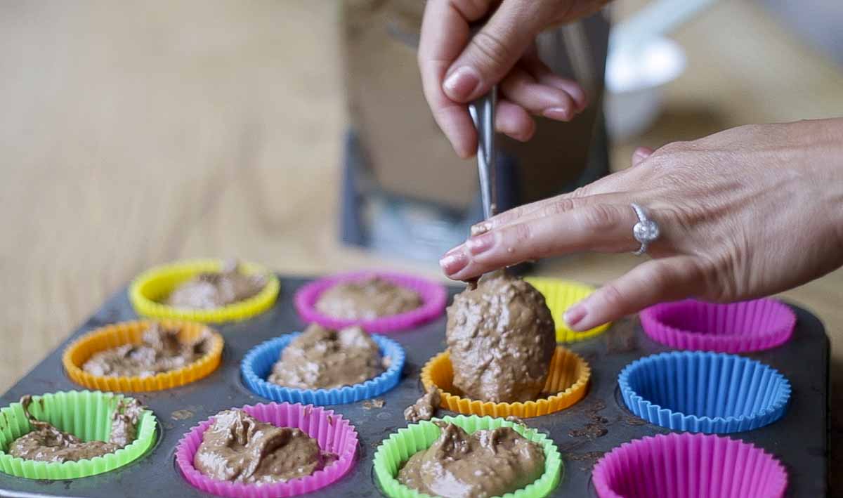 hand adding grain free chocolate muffin batter to colorful silicon cups in a muffin tin